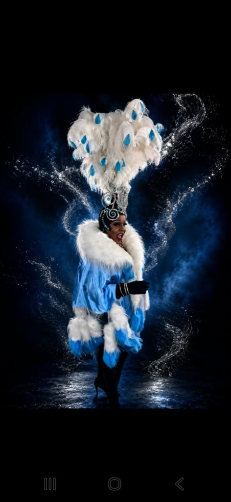 Artiste en cape bleu ciel, coiffe de plumes blanches et bleues