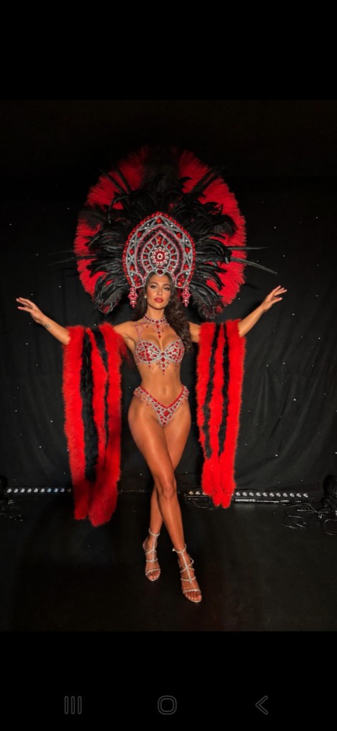 Danseuse en costume de plumes rouges et noires, bras ouverts sur scène